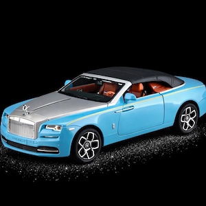 Peut inclure: Modèle de voiture Rolls-Royce décapotable bleu clair avec capot argenté et toit noir. L'intérieur est beige et les roues noires et blanches. Le logo Rolls-Royce est visible sur le capot.