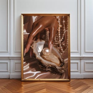 Può includere: Una stampa artistica da parete incorniciata che mostra una mano dalla pelle scura con lunghe unghie chiare che tiene una singola perla bianca lucente all'interno di un'ostrica aperta. Diverse collane di perle bianche pendono sulla mano e sul polso.