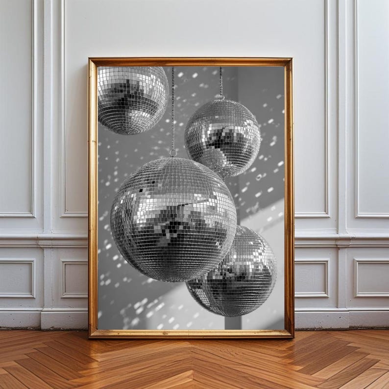 K&ouml;nnte beinhalten: Ein gerahmter Kunstdruck mit vier silbernen Discokugeln unterschiedlicher Gr&ouml;&szlig;e, die in der Luft h&auml;ngen. Die kugelf&ouml;rmigen Objekte sind mit kleinen, reflektierenden Spiegelkacheln bedeckt, die das Licht einfangen und streuen.