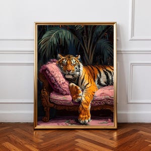 Könnte beinhalten: Gerahmter Kunstdruck mit einem Tiger, der sich auf einer rosa Chaiselongue ausruht. Der Tiger hat orange und schwarze Streifen. Die Chaiselongue hat verzierte Holzdetails und rosa Kissen. Der Hintergrund zeigt üppiges grünes Laub.