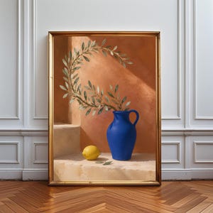 Può includere: Una stampa d'arte incorniciata raffigurante una brocca in ceramica blu brillante appoggiata su una superficie in pietra accanto a un limone giallo. Un ramo d'ulivo curvo con foglie verdi sporge dalla brocca su uno sfondo caldo color terracotta.
