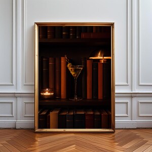 May include: A framed rectangular wall art print featuring a dark wooden bookshelf filled with rows of leather-bound books in shades of brown and black. A martini glass with olives sits on a shelf next to a small glowing lamp and a lit candle.