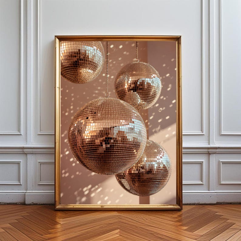 K&ouml;nnte beinhalten: Ein gerahmter Kunstdruck mit vier kugelf&ouml;rmigen Discokugeln mit reflektierenden goldenen Spiegeloberfl&auml;chen. Die Discokugeln h&auml;ngen in unterschiedlichen H&ouml;hen vor einem sanften pfirsichfarbenen Hintergrund und erzeugen verstreute Lichtreflexe.