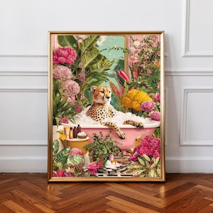 Op de afbeelding: Een ingelijste kunstdruk toont een cheetah in een roze badkuip met bubbels, omringd door tropische planten en bloemen. Het kunstwerk heeft een gouden lijst. De bloemen zijn roze en geel.