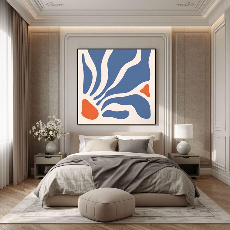 May include: A square wall art piece featuring an abstract design with organic, flowing blue shapes on a cream background, accented by two solid orange shapes, all enclosed within a thin black frame, displayed above a bed in a bedroom.