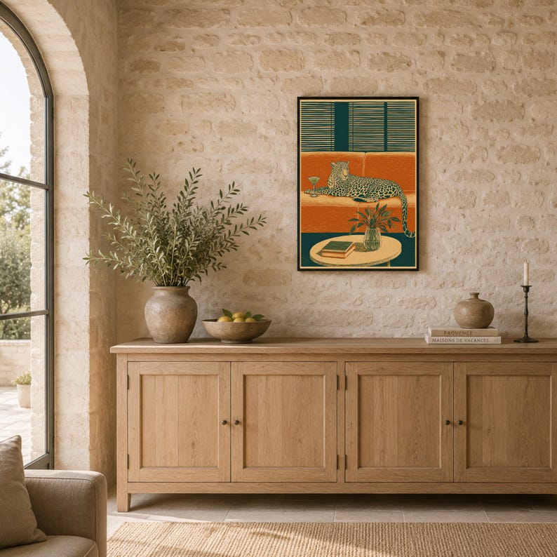 Peut inclure: Une impression d'art mural rectangulaire dans un cadre noir repr&eacute;sentant une illustration stylis&eacute;e d'un l&eacute;opard allong&eacute; sur un canap&eacute; orange avec un verre &agrave; martini, devant des stores vert fonc&eacute;, avec une table, une plante et un livre.