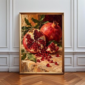 Pode incluir: Uma pintura a óleo emoldurada retratando duas romãs, uma inteira e outra aberta, revelando sementes vermelho-escuras. A fruta repousa sobre uma superfície de pedra texturizada com folhas verdes espalhadas, em tons quentes de vermelho, ouro e castanho.