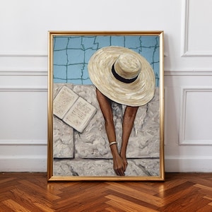 Puede incluir: Pintura enmarcada que representa a una persona con un sombrero de paja grande, cerca de una piscina. Un libro abierto descansa sobre una superficie de piedra. La obra tiene un marco dorado y un fondo de piscina azul.