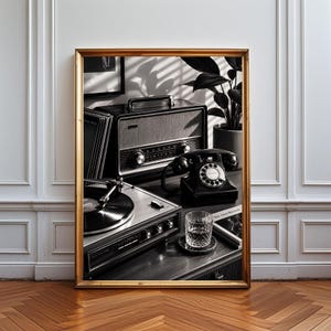 Könnte beinhalten: Ein gerahmter Wandkunstdruck mit einer schwarz-weißen Komposition aus einem Vintage-Radio, einem Wählscheibentelefon, einem Plattenspieler und einem Glas Wasser. Die Szene zeigt eine nostalgische Anordnung analoger Technik und ein Buch.