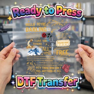 May include: A clear DTF transfer sheet with the text "Ready to Press" and "DTF Transfer" in a colorful font. The sheet features gold and white text, a rose, a sword, a feather, and other graphics. The text includes phrases like "Hello Feyre Darling" and "I Love You... Thorns and All."
