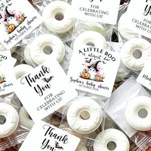 May include: White ring-shaped candies in clear plastic bags with square labels featuring a ghost in a witch hat, pumpkins, bats, and the text A LITTLE BOO IS ALMOST DUE, a baby shower name, October 2026, and THANK YOU FOR CELEBRATING WITH US.