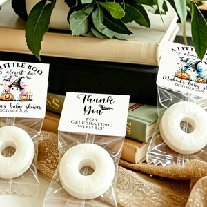 May include: Three clear plastic bags containing white ring-shaped candies, each sealed with a white paper topper. Two toppers feature a ghost in a witch hat with pumpkins and the text A LITTLE BOO is almost due. One topper says THANK YOU.