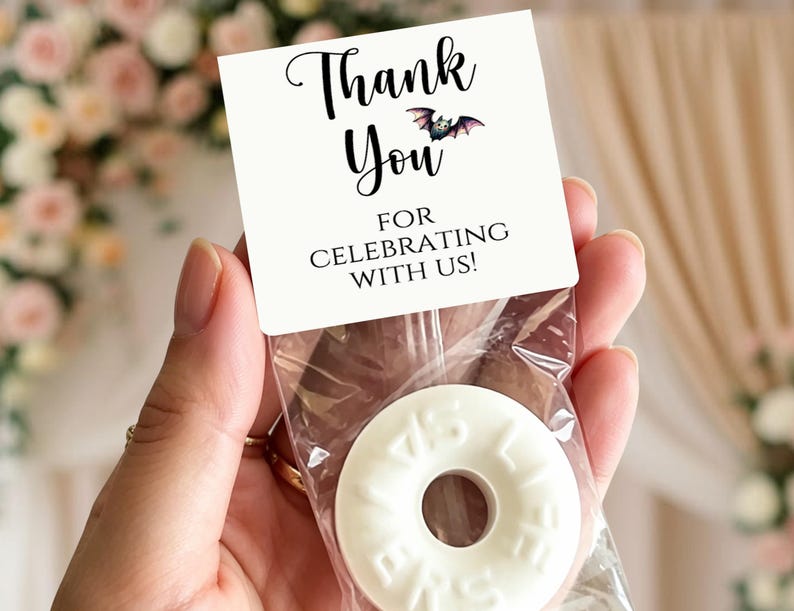 May include: A clear plastic favor bag containing a white ring-shaped candy with embossed text. The bag is sealed with a white cardstock topper featuring the black printed text Thank You For Celebrating With Us and a small illustration of a bat.