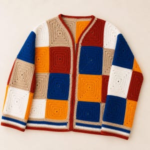 K&ouml;nnte beinhalten: Eine lang&auml;rmelige Strickjacke aus mehreren quadratischen H&auml;kelaufn&auml;hern in einer lebendigen Farbpalette aus K&ouml;nigsblau, Senfgelb, Terrakotta-Rot, Beige und Wei&szlig;. Das Kleidungsst&uuml;ck hat einen V-Ausschnitt und einen geraden Saum mit Streifendetails.