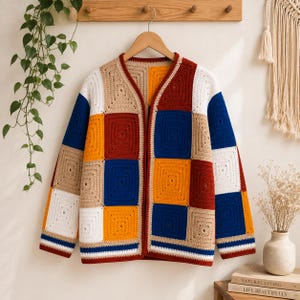 K&ouml;nnte beinhalten: Eine lang&auml;rmelige Strickjacke aus mehrfarbigen H&auml;kel-Granny-Squares in den Farben Dunkelrot, leuchtendes Blau, Senfgelb, Wei&szlig; und Beige. Das Kleidungsst&uuml;ck hat einen V-Ausschnitt, eine offene Vorderseite und einen gestreiften Saum in Blau und Wei&szlig;.