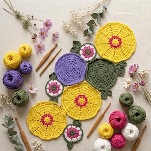 May include: A collection of handmade crochet items, including yellow, purple, and green coasters, along with crochet hooks and balls of yarn in various colors. The coasters have a floral design. The image also includes flowers.