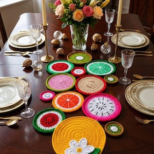 May include: A collection of round, crocheted coasters featuring various fruit designs including watermelon, orange, kiwi, and dragon fruit, arranged on a dark wooden table alongside white plates, gold cutlery, crystal glasses, and a flower bouquet.