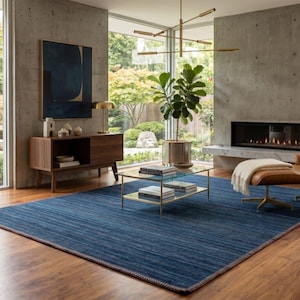 Puede incluir: Un sal&oacute;n moderno con una alfombra azul, un sill&oacute;n de cuero y una chimenea. La habitaci&oacute;n cuenta con grandes ventanales con vistas a un jard&iacute;n, un mueble de madera y una mesa de centro de cristal.