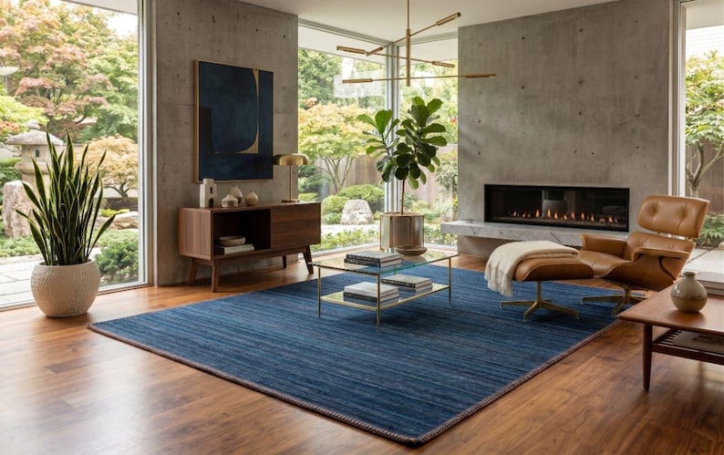 Puede incluir: Un sal&oacute;n moderno con una alfombra azul, un sill&oacute;n de cuero y una chimenea. La habitaci&oacute;n cuenta con grandes ventanales con vistas a un jard&iacute;n, un mueble de madera y una mesa de centro de cristal.
