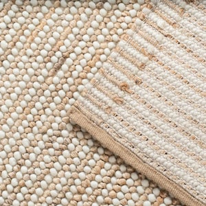 May include: Close-up of a textured rug in beige and off-white. The rug has a combination of woven and bobble textures, creating a visually interesting pattern. The edges are finished with a beige border.