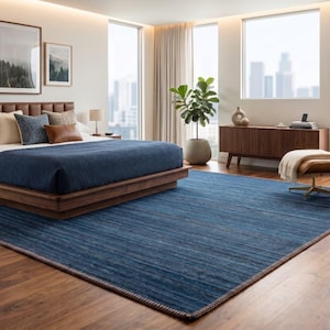 Puede incluir: Un dormitorio moderno con una cama grande, una alfombra azul y un sill&oacute;n de cuero. La cama tiene un cabecero marr&oacute;n y un edred&oacute;n azul. La alfombra es rectangular y tiene un dise&ntilde;o azul y marr&oacute;n. El sill&oacute;n es de cuero marr&oacute;n.