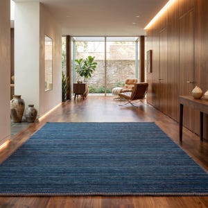 Puede incluir: Una alfombra azul rectangular con superficie texturizada sobre un suelo de madera en un pasillo. La alfombra est&aacute; centrada en el espacio, con un borde claro. El pasillo presenta paneles de madera, una mesa y una pintura. Dimensiones: 300cm x 200cm.