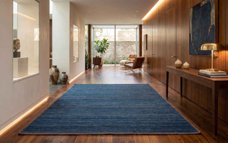 Puede incluir: Una alfombra azul rectangular con superficie texturizada sobre un suelo de madera en un pasillo. La alfombra est&aacute; centrada en el espacio, con un borde claro. El pasillo presenta paneles de madera, una mesa y una pintura. Dimensiones: 300cm x 200cm.