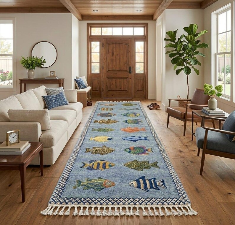 May include: A long, rectangular blue rug with a repeating pattern of colorful fish. The rug has a white fringe along the short ends and is placed in a hallway with hardwood floors and a wooden door.