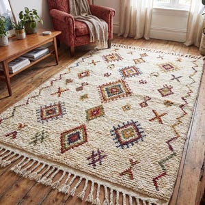 May include: A rectangular area rug with a cream-colored base featuring a textured, shaggy pile. The rug is decorated with a repeating pattern of colorful geometric shapes, including diamonds and crosses in red, blue, yellow, and green, finished with knotted fringe.