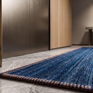 Puede incluir: Una alfombra rectangular azul y marr&oacute;n con una superficie texturizada. La alfombra est&aacute; colocada sobre un suelo de m&aacute;rmol. La alfombra tiene un borde marr&oacute;n y est&aacute; frente a un mueble de madera.