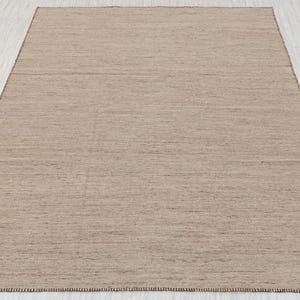 A full, straight-on view of a rectangular beige flatweave rug with brown stitched edges, laid on a light-colored floor.