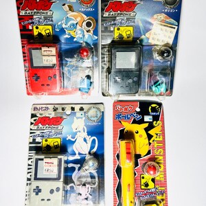 May include: Four packaged Battpoke Pocket Monsters toys by Tomy. Three sets include a handheld game console replica and a small character figure. One set features a yellow pen with a Pikachu graphic and a small red ball and yellow figure.
