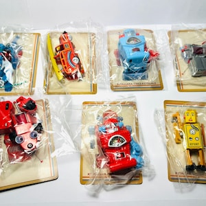 Op de afbeelding: Verzameling vintage speelgoedrobots in plastic verpakking. De robots zijn in verschillende kleuren, waaronder blauw, rood, geel en grijs. Elke robot is bevestigd aan een kartonnen achterkant met de tekst "KITAHARA COLLECTION".