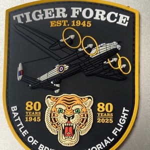 Może przedstawiać: Czarna i żółta naszywka z napisem "TIGER FORCE EST. 1945" i ilustracją bombowca. Naszywka zawiera również głowę tygrysa i napis "80 YEARS 1945-2025 BATTLE OF BRITAIN MEMORIAL FLIGHT".