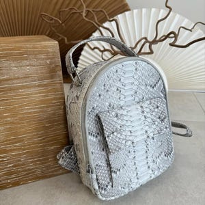 Może przedstawiać: Zestaw trzech ceramicznych kubków z nakrapianym, matowym wykończeniem. Kubki są w odcieniach kremu, jasnoszarym i ciemnoszarym. Każdy kubek ma prosty, minimalistyczny design i zaokrąglony uchwyt.