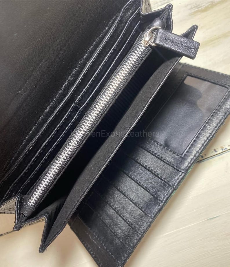 Puede incluir: Cartera de cuero negro abierta con m&uacute;ltiples compartimentos, incluyendo ranuras para tarjetas y una secci&oacute;n con cremallera. La cartera est&aacute; abierta, revelando el dise&ntilde;o interior. La cremallera es plateada.