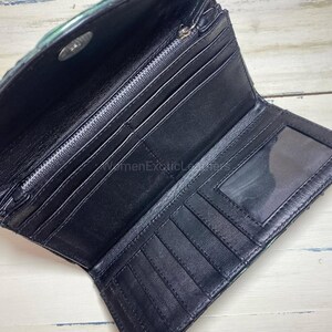 Puede incluir: Cartera de cuero negro abierta con m&uacute;ltiples ranuras para tarjetas, un compartimento con cremallera y una ventana de identificaci&oacute;n transparente. La cartera tiene un exterior texturizado, te&ntilde;ido de verde y un cierre a presi&oacute;n plateado. El interior es negro.