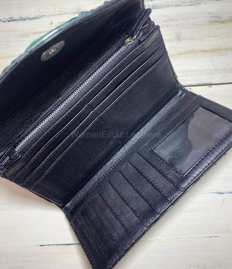 Puede incluir: Cartera de cuero negro abierta con m&uacute;ltiples ranuras para tarjetas, un compartimento con cremallera y una ventana de identificaci&oacute;n transparente. La cartera tiene un exterior texturizado, te&ntilde;ido de verde y un cierre a presi&oacute;n plateado. El interior es negro.