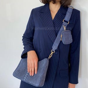 May include: A blue leather shoulder bag with a matching strap and small pouch. The bag features a snakeskin pattern and gold-coloured hardware. The strap is adjustable. The bag is worn over the shoulder.