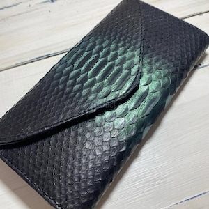 May include: A black leather wallet with a snakeskin texture and a flap closure. The wallet has a gradient of green and black hues. The wallet is rectangular and appears to be made of genuine leather.