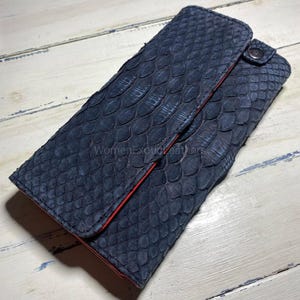 May include: A dark blue wallet with a scale-like texture. The interior is red, and it fastens with a snap. The text "WomenExoticLeathers" is visible on the wallet.
