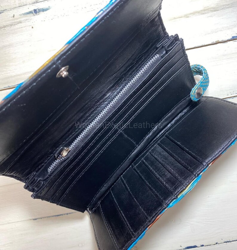 K&ouml;nnte beinhalten: Ge&ouml;ffnete schwarze Ledergeldb&ouml;rse mit mehreren Kartenf&auml;chern und einem Rei&szlig;verschlussfach. Die Au&szlig;enseite weist ein farbenfrohes Muster mit Blau-, Gelb- und Oranget&ouml;nen auf. Die Geldb&ouml;rse ist ge&ouml;ffnet und zeigt die Innenf&auml;cher.