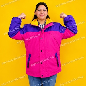 Könnte beinhalten: Eine farblich abgesetzte Winterjacke mit einem leuchtend pinken Unterteil, einem violetten Oberteil und Ärmeln sowie einem gelben Innenkragen. Die Jacke verfügt über eine Knopfleiste auf der Vorderseite, lange Ärmel und zwei Seitentaschen.
