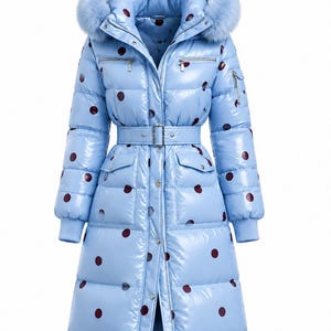 May include: A light blue, glossy, knee-length puffer coat featuring a dark red polka dot pattern. The coat includes a hood with a light blue faux fur trim, a matching belt with a buckle, two chest zipper pockets, and two front flap pockets.