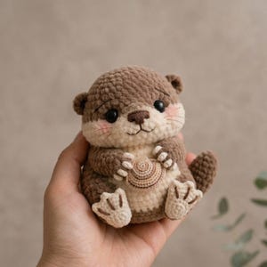 May include: A handmade crochet otter plushie in shades of brown and cream, holding a small, crocheted seashell. The otter has black eyes, pink cheeks, and detailed paws. A charming, soft toy.