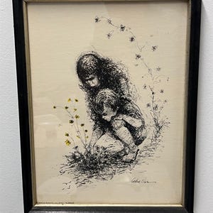 May include: Black framed pen and ink drawing of two children, one kneeling and the other seated, picking flowers. The artwork features delicate linework and a neutral color palette, with yellow flowers adding a pop of color. The artwork is signed.