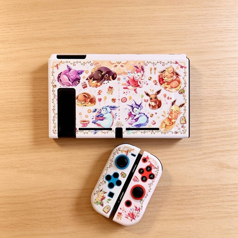 May include: White Nintendo Switch console and Joy-Cons featuring a colorful illustration of various cartoon characters. The console has a decorative border and the Joy-Cons have blue and red buttons.