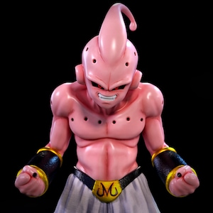 Puede incluir: Una figura rosa de un personaje musculoso con una cabeza distintiva en forma de antena y múltiples agujeros negros en el cuerpo. El personaje tiene una expresión severa, ojos rojos y una sonrisa con dientes blancos. Brazaletes negros y dorados y un cinturón con una "M" dorada completan el look.