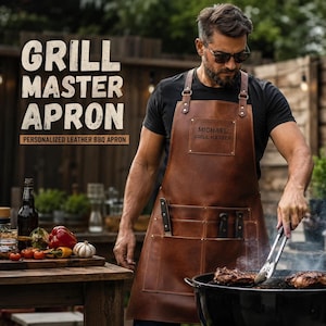 May include: A brown leather apron featuring a rectangular chest patch with the text MICHAEL GRILL MASTER, multiple front pockets, and metal rivets. The apron includes adjustable shoulder straps and is worn while using metal tongs over a grill.