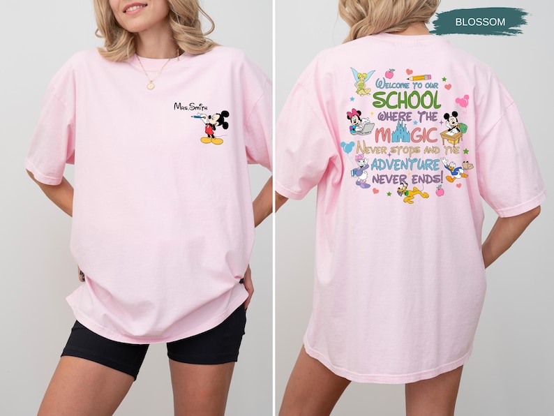 May include: A light pink t-shirt featuring Mickey Mouse with the text "Mrs. Smith" on the front. The back of the shirt has a colorful graphic with Disney characters and the words "Welcome to our school where the magic never stops and the adventure never ends!"